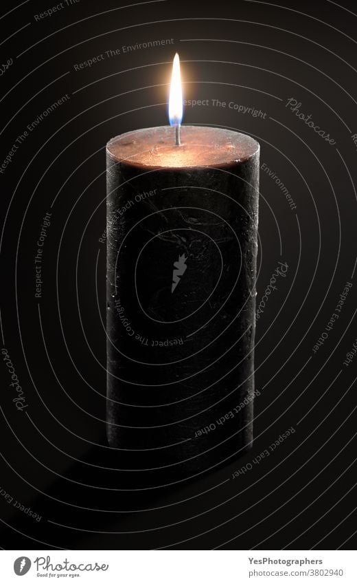 Black candle with a glowing flame isolated on a black background. Burning candle close-up advent aromatic black candle burn burning candlelight celebration