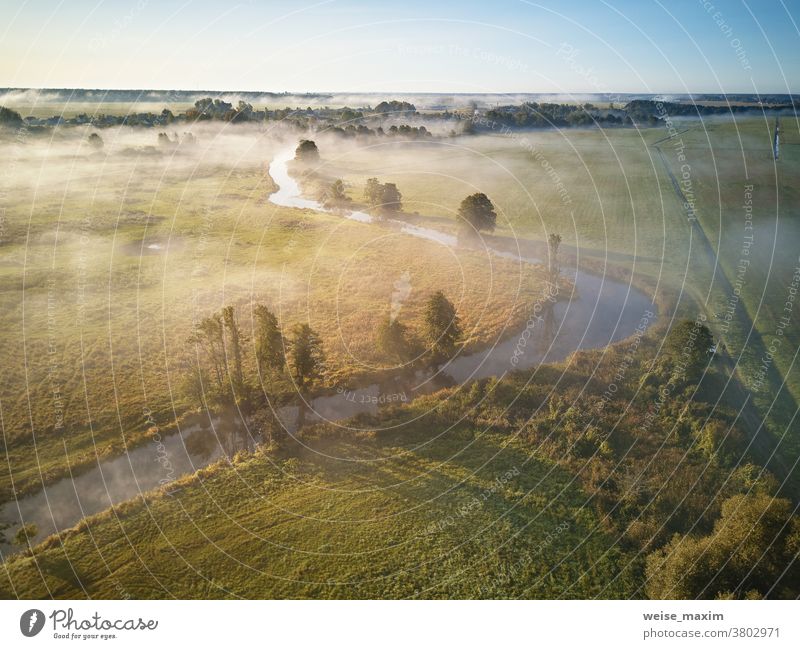 Autumn foggy sunrise aerial view. Small river with trees in meadow and field nature autumn water forest morning sunlight landscape background fall dawn mist