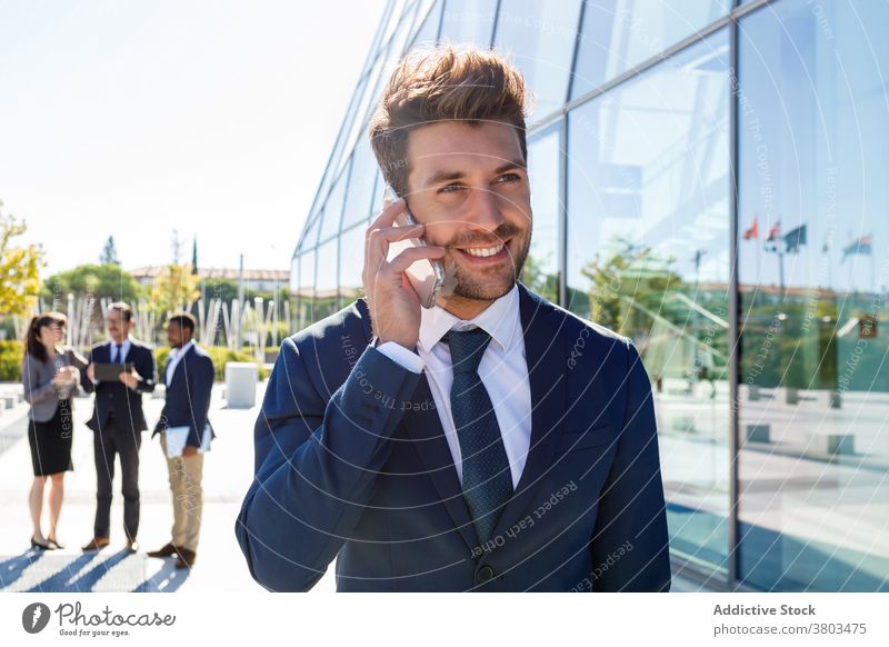 Happy young businessman talking on smartphone on street conversation communicate classy confident entrepreneur call building exterior male suit executive formal