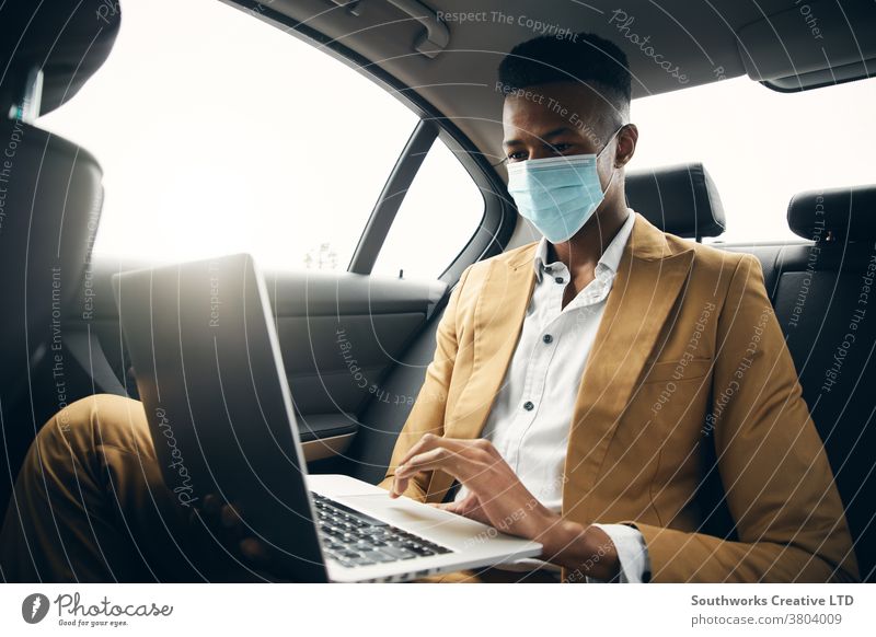 Young Businessman Wearing Mask Working On Laptop In Back Of Taxi During Health Pandemic business businessman taxi face mask face covering wearing ppe cab car