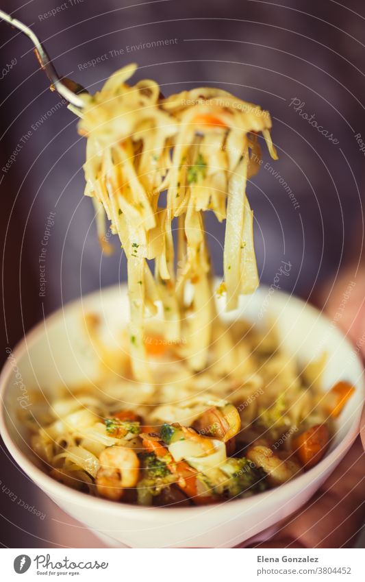 Hand uses fork to pickup tasty noodles with vegetables and shrimp on dark background. Asian food concept bowl chinese onion pasta dishes pepper spicy carrots