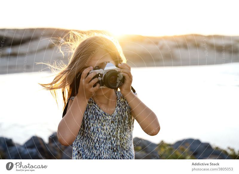 Anonymous lady shooting sea on photo camera during summer vacation woman take photo tourist sunset style holiday shore rocky travel female young dress trendy