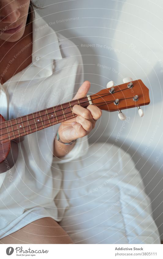 Anonymous woman laying ukulele on bed play allure sensual musician song perform rest comfort morning female young gorgeous white shirt melody enjoy acoustic