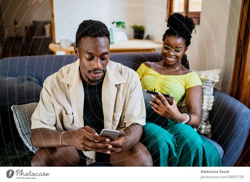 Young ethnic couple using gadgets while relaxing on couch at home sofa together relationship tablet smartphone addict connection browsing online internet