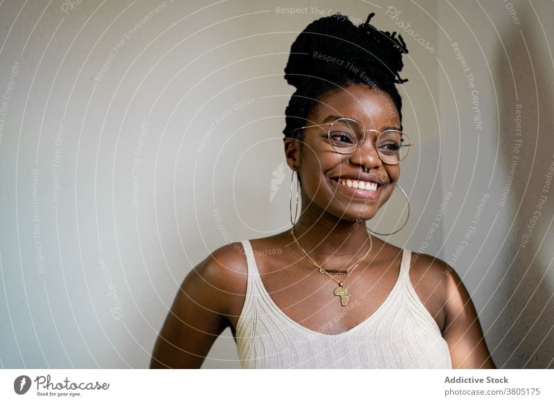 Happy black woman in eyeglasses in room toothy smile hairstyle accessory fashion outfit content cheerful female african american happy brunette joy positive