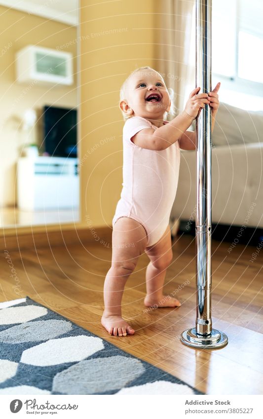 Cute baby standing on floor and laughing cheerful pole home happy joy step childhood positive delight glad daylight infant girl bodysuit blond enjoy apartment