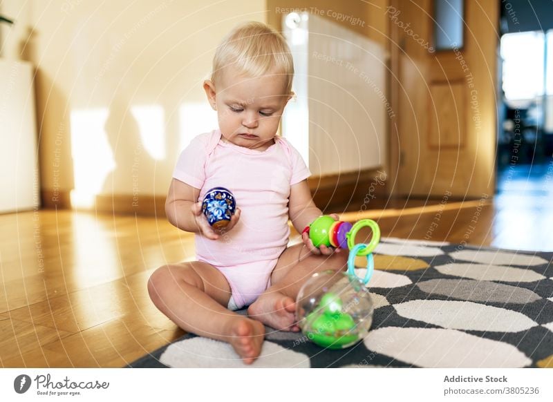 Cute infant playing with toys on floor baby interest cute innocent game home childhood curious playful joy girl barefoot carpet apartment sunlight babyhood
