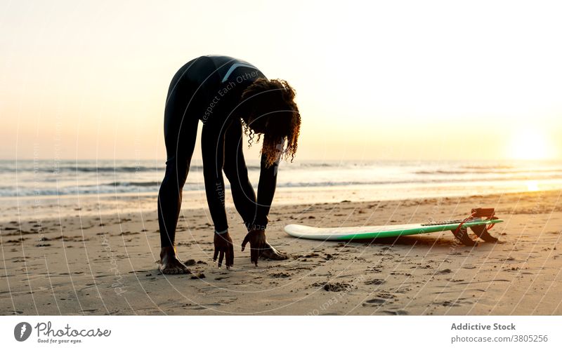 Unrecognizable black surfer stretching on coast of ocean man surfboard sea break water sports skimboard beach male curly hair ethnic summer vacation seaside