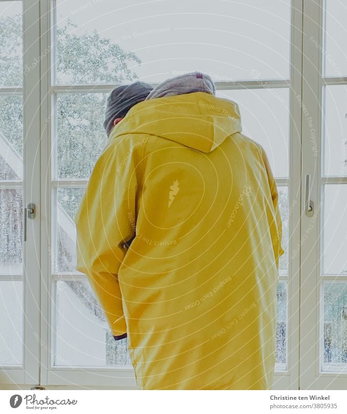 Man stands at the window in rainy weather and puts on a Frisian mink | trapped in plastic friesennerz Rain jacket Raincoat Rainy weather Bad weather