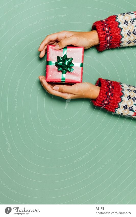 Female hands with a winter sweater holding a Christmas gift on a green background. box present giving receiving package top view surprise high angle view give
