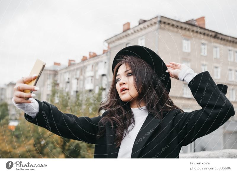 Young asian female in dark coat and hat taking a selfie outdoors mobile photo woman lady camera smartphone girl lifestyle young fun picture beautiful portrait