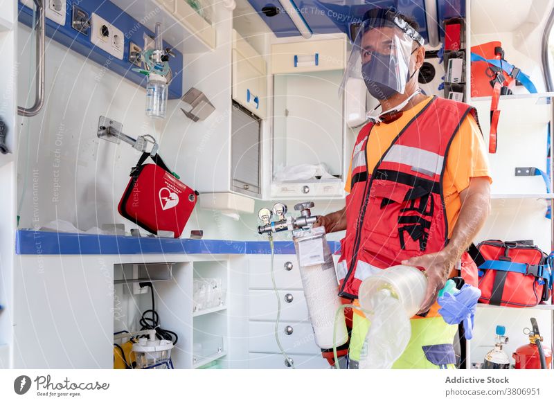 Anonymous lifeguard in visor with medical equipment in ambulance protective shield uniform profession work car worker first aid kit professional mask roll man