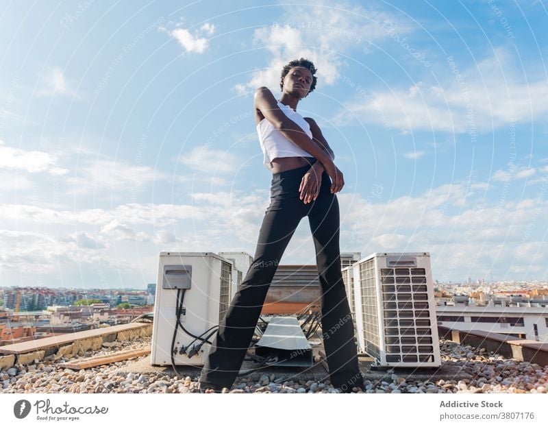 Stylish black female model standing graciously on rooftop woman style appearance confident outfit cool glamour calm slender positive serene unemotional sensual