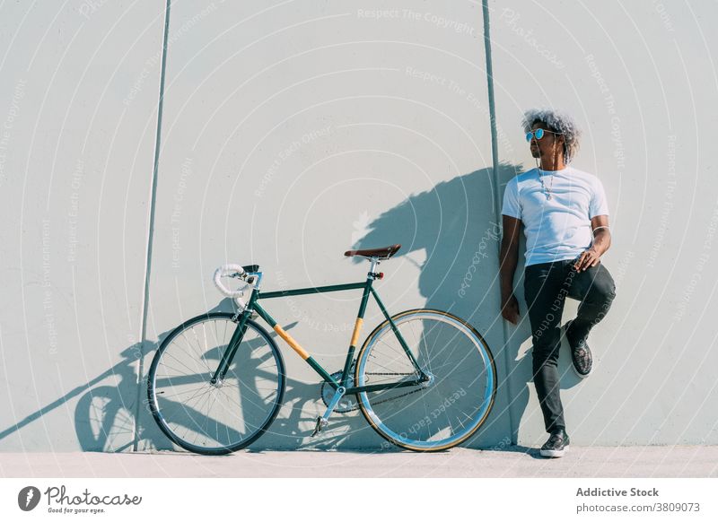 Black cyclist leaning against a gray wall next to his city bike. black cyclist rider black rider bycicle afro black man sustainable transport riding