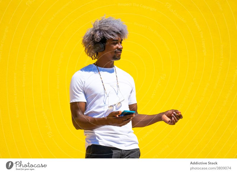 Black man with afro hair listening to music with headphones and black man listen to music earphones dancing dance dancing teacher yellow background casual