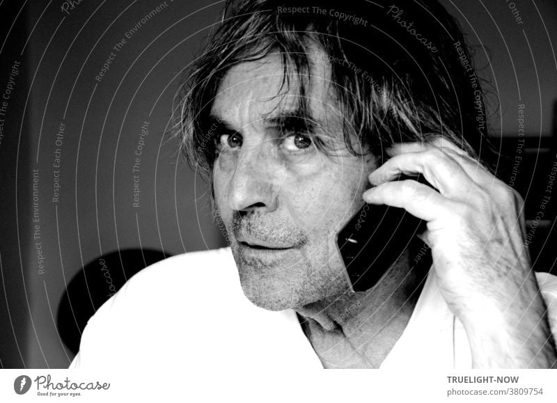 Don't disturb me when I'm talking on the phone, the somewhat wild looking, unshaven man with long hair in half profile and white T-shirt seems to think while holding a cordless phone to his ear