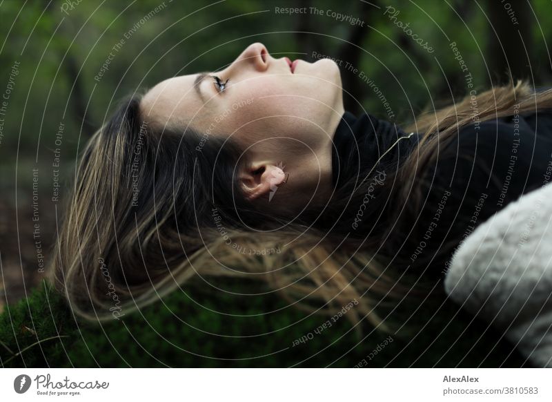 Lateral portrait of a young woman lying on a moss hill in the forest and looking up Woman 18 - 30 years pretty fit Slim smart Pleasant Attractive Brunette