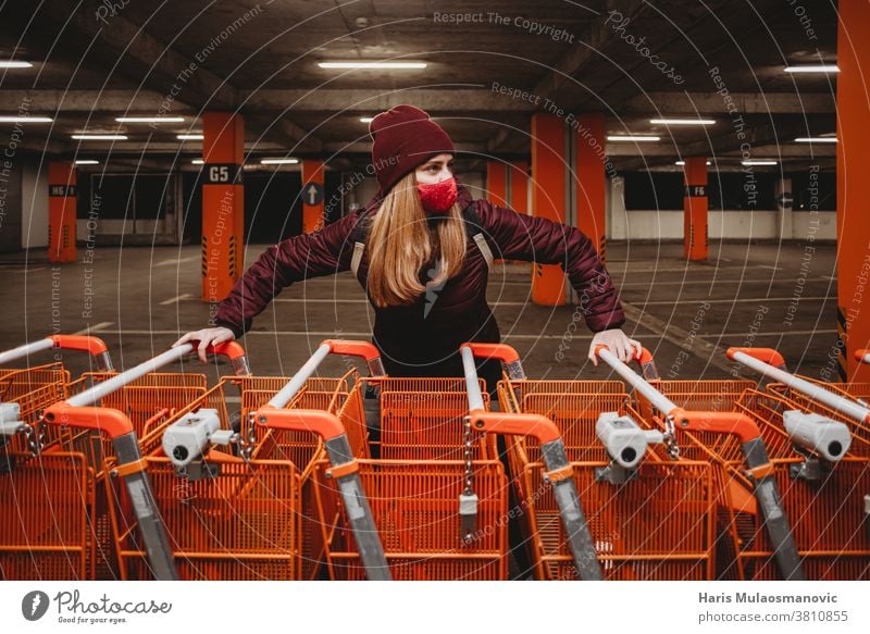 Woman with mask holding row of orange shopping carts in garage attractive bag beautiful big shopping carts car park caucasian city clothes cold collection
