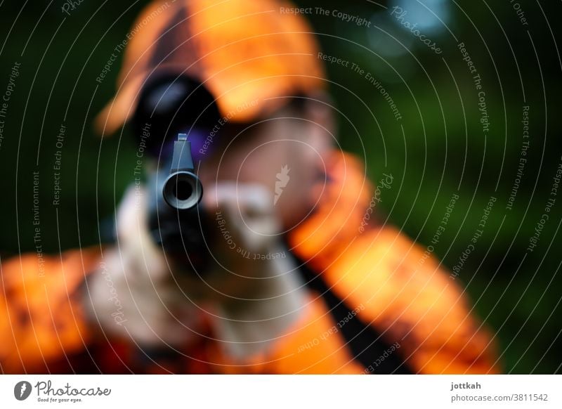 View into the barrel of a hunting rifle held by a hunter dressed in orange. The focus is on the muzzle of the gun. Hunting Hunter Orange Weapon Rifle Shotgun