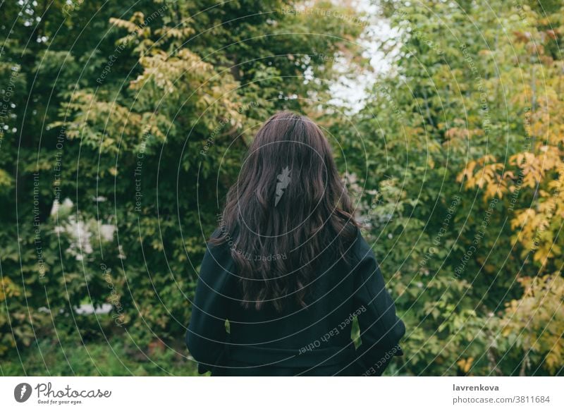 Portait from the back of female in dark coat outdoors in park or forest alone cold woman beautiful hair fall trees adult jacket autumn walking faceless