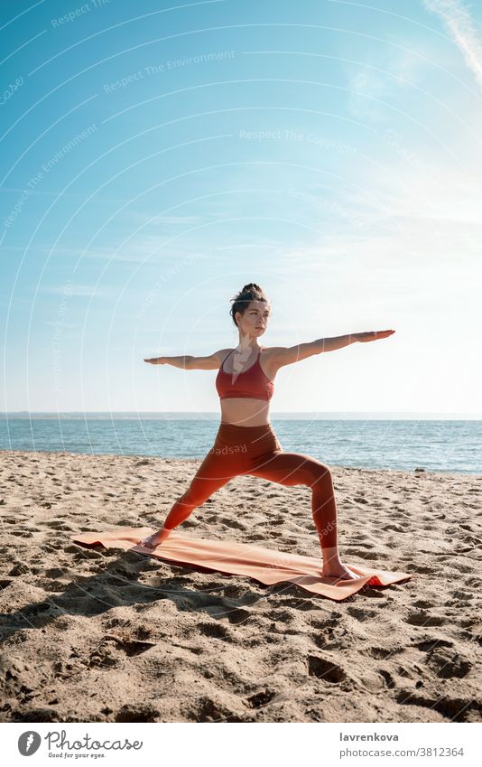 Young adult female practising yoga on a beach, Virabhadrasana II pose exercise training sea healthy athletic woman activity relaxation fitness lifestyle workout