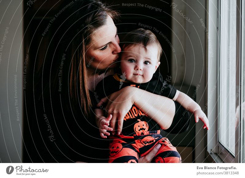 young mother and baby girl at home looking by the window. Baby girl wearing Halloween clothes. Family lifestyle indoors love together family childhood