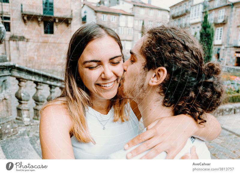 Young man kissing his girlfriends while she smiles adult feeling white fun portrait pose woman hugging boyfriend young couple hold happiness grin caucasian