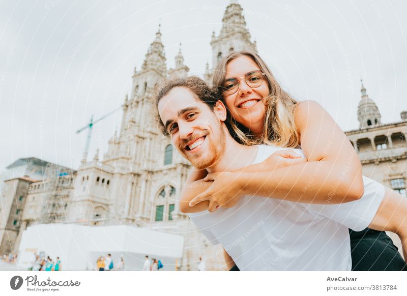 Young couple smiling to camera with the woman over the man in front of a touristic place casual joyful trip outdoors tourism vacations adults people male