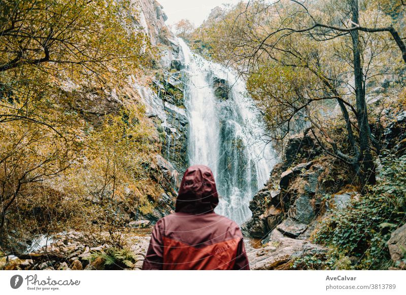 Woman out of focus in a purple oilskin standing in front of a giant waterfall backpack outdoors forest people looking view female white adventure sunny