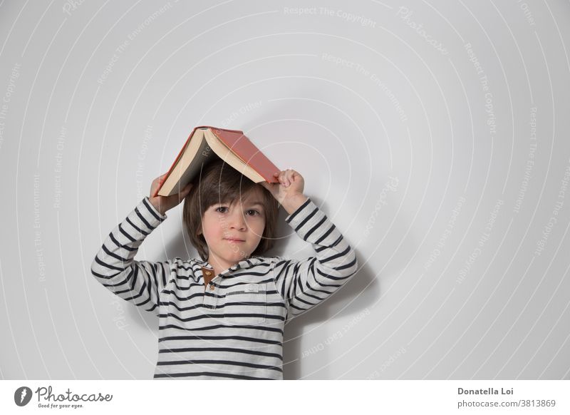 Child portrait with book on the head adorable boy caucasian cheerful child childhood cute day education emotion expression face fun happiness happy holding