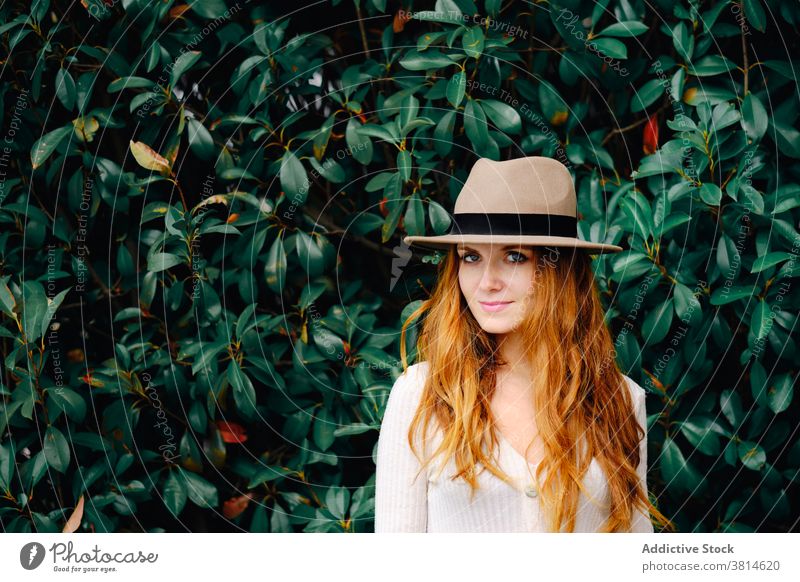 Young woman in hat standing in garden style redhead trendy red hair modern ginger vogue young female fashion long hair lady confident charming lifestyle elegant