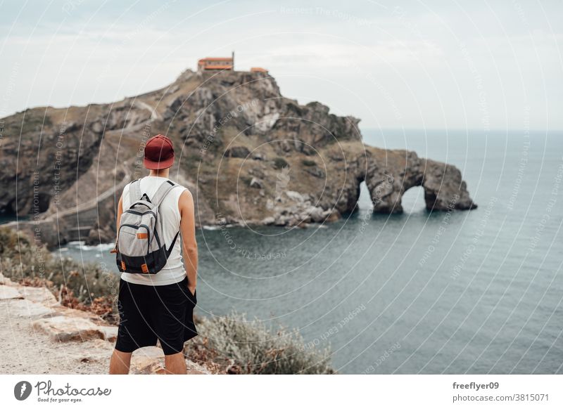 Young man with a hat in front of the Gaztelugatxe Island one tourist backpacker tourism visiting sightseeing romantic island vizcaya spain bermeo X century