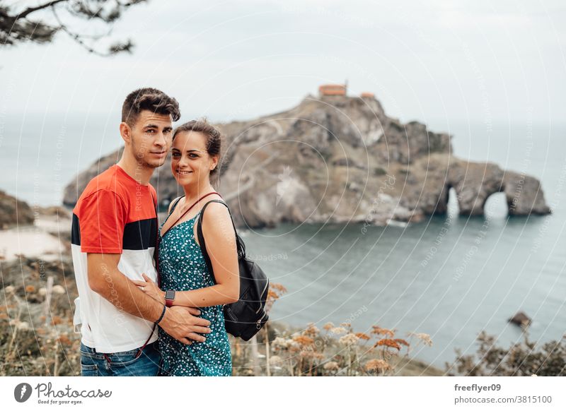 Young couple in front of Gaztelugatxe Island tourists tourism visiting sightseeing sightseers romantic island vizcaya spain bermeo X century copy space travel