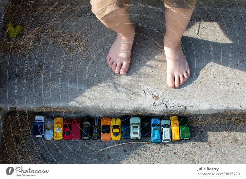 Toy cars in a row on concrete stairs near child's feet; outdoor play toy car toy cars Playing Playful Toes Concrete Line lined up Row free play candid childhood