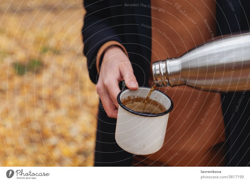 Closeup of female hands pouring hot tea into enamel cup outdoors mug hiking drinking smiling leisure thermos picnic travel activity camping autumn faceless