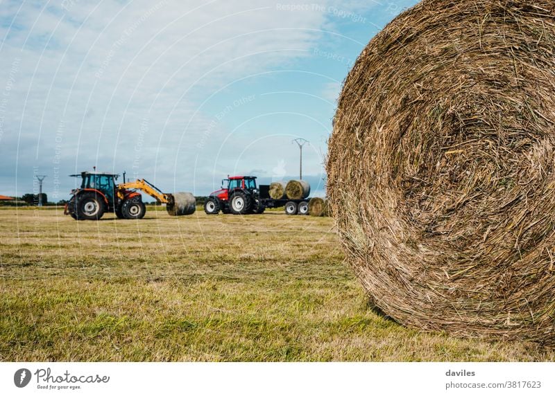 Rounded straw bale and two tractors working in the background harvesting campaign package grassland scenery vehicle machine compactor pile agricultural autumn