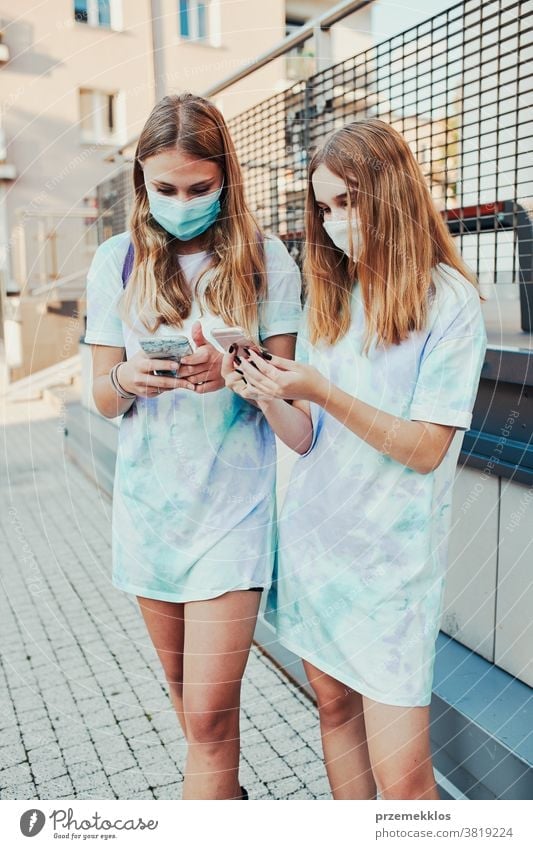 Young women using smartphone wearing the face masks to avoid virus infection standing in a street caucasian cellphone conversation covid-19 female lifestyle