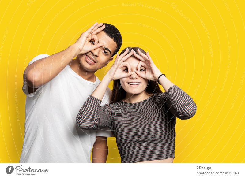 Portrait of funky cheerful couple making binoculars with fingers wearing casual shirts isolated on bright yellow background relax 2 comic playful laughter