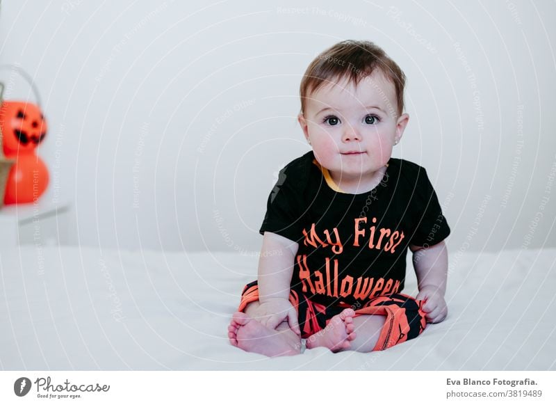 cute baby girl in halloween costume at home, sitting on bed with Halloween decoration, Lifestyle indoors trick or treat pumpkin balloons orange october house