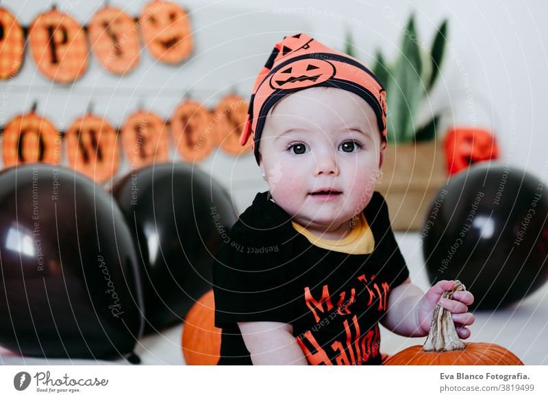 cute baby girl in halloween costume at home, sitting on bed with Halloween decoration, Lifestyle indoors trick or treat pumpkin balloons orange october house