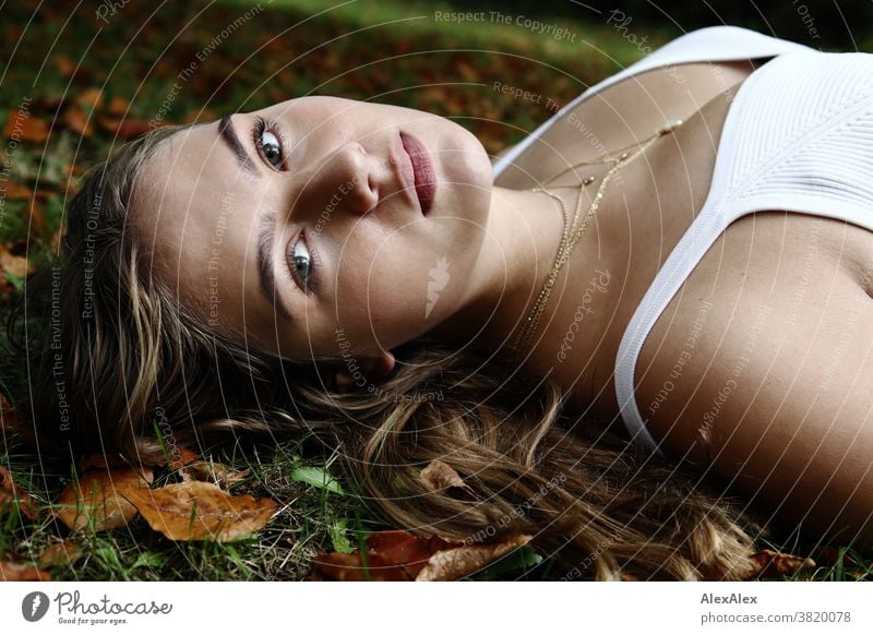 Lateral portrait of a girl in a white strap top lying on an autumn meadow with leaves Landscape Beach Intensive teen kind Nature feminine Uniqueness Exceptional