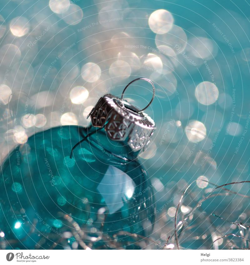 Christmas glitter - turquoise blue glass Christmas ball with silver hanger in front of turquoise white background with bokeh christmas ball Glass ball