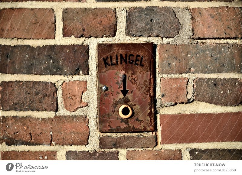 Brick or brick wall of a functional building with a built-in bell on a rusty iron plate in which the word bell and an arrow to the bell button is carved.