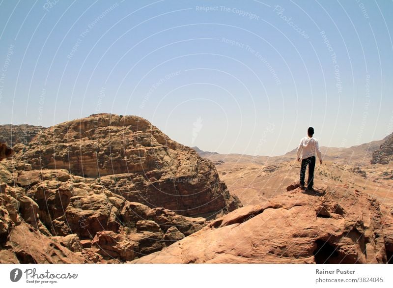 Young man on top of a peak looking over a valley in the rugged landscape of Petra, Jordan adventure copy space desert explore the world explorer future concept