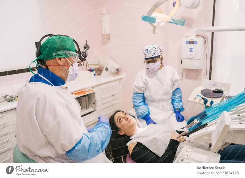 Unrecognizable dentist and nurse interacting with female patient in clinic equipment medical stomatology professional uniform orthodontist health care together