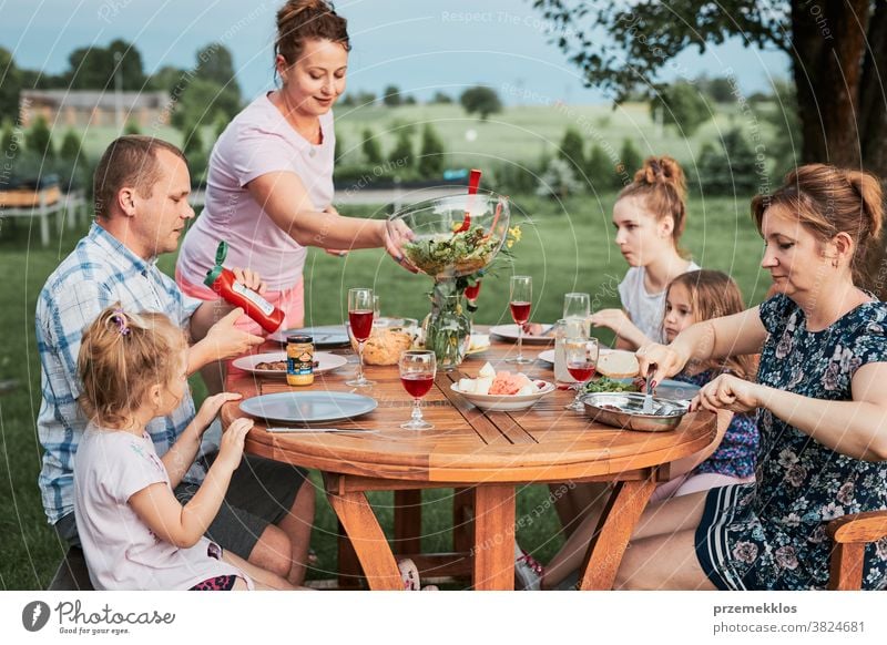 Family having a meal during summer picnic outdoor dinner in a home garden feast food man together woman child barbecue table eating gathering people lifestyle