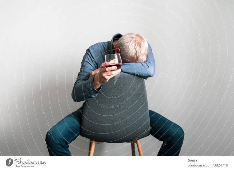 Depressed man sitting on an armchair with his head on one arm and a glass of cognac in his hand Man depression Distress Loneliness sad unhappy Lonely Armchair