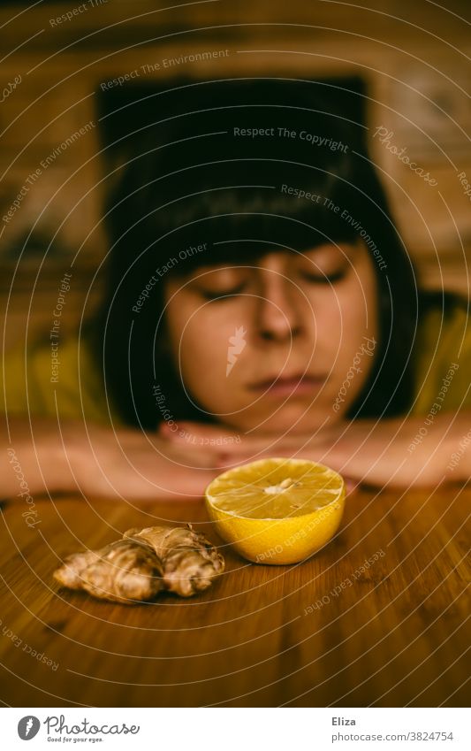 A woman is tired, limp and cold and lies with her head on the table behind ginger and lemon. Common cold listless Ginger Sick Lemon immune system