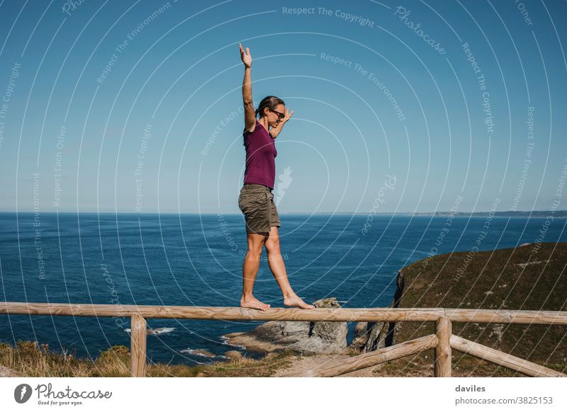 Woman walking and balancing on a wooden railing at the coast line. athletic outdoor lifestyle vacation summer sea person water balance travel standing holiday