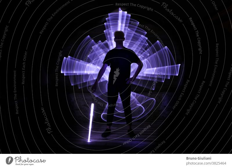 Silhouette of a man standing with a lightsaber with neon drawings and leds at lightpainting. silhouette abstract art boy bright energy curve dark design effect